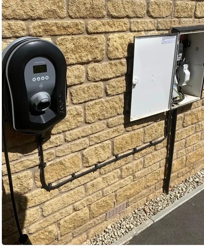 A Zappi EV charge point and its isolator mounted on a stone wall, with the cable run clipped in conduit down to the unit